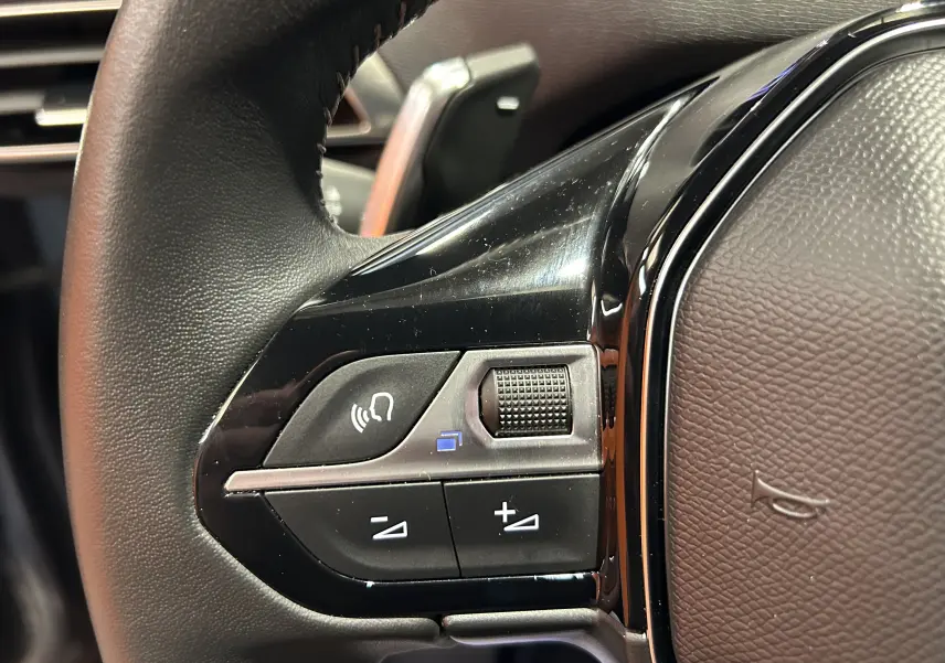 Détail du volant noir du Peugeot 3008 Hybrid 2024 montrant les commandes audio et téléphone côté gauche.
