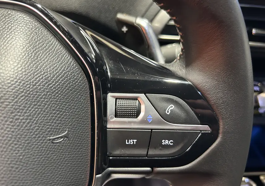 Détail du volant cuir du Peugeot 3008 Hybrid 2024 montrant les commandes audio et téléphone côté gauche.