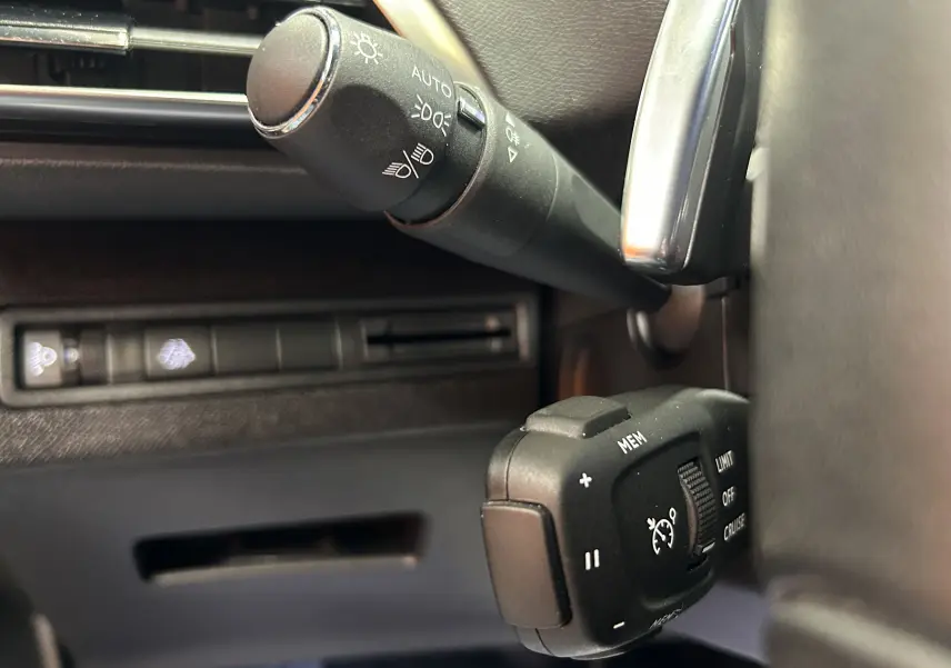 Gros plan sur les commandes de régulateur de vitesse et éclairage du Peugeot 3008 Hybrid gris, côté gauche du volant.