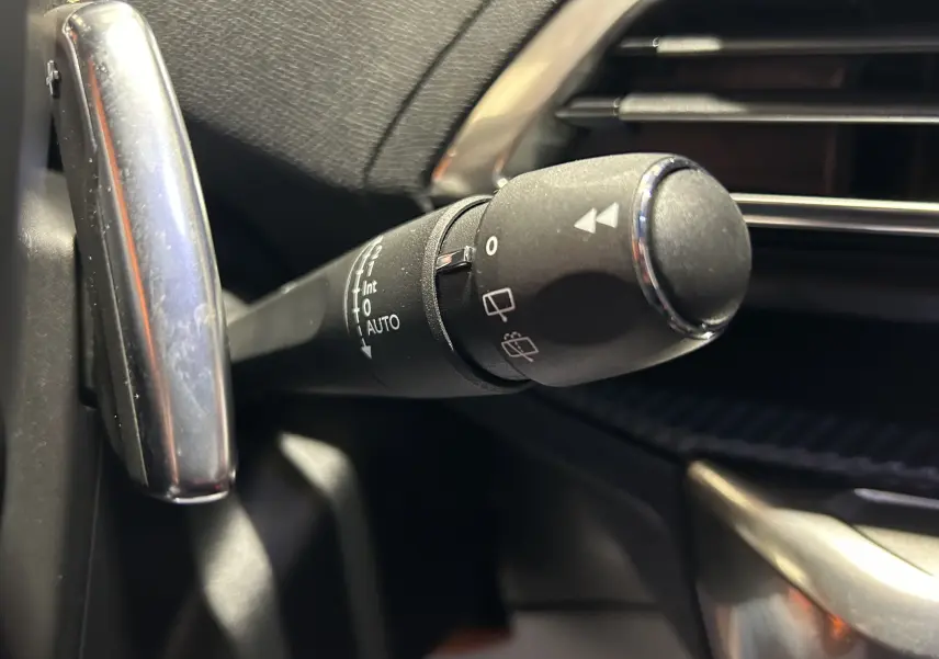 Gros plan sur la commande d’essuie-glace noire avec marquages blancs dans l’habitacle du Peugeot 3008 gris 2024.