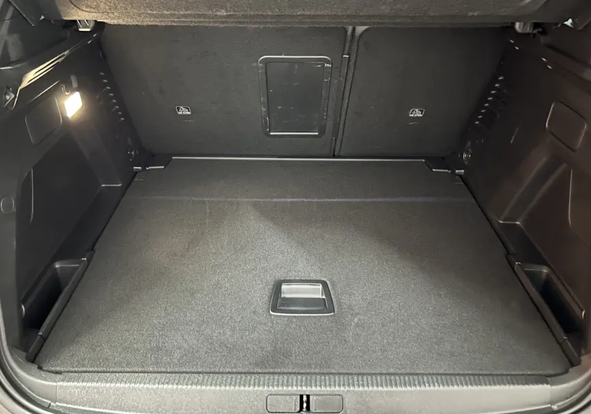 Coffre ouvert en vue arrière d’un Peugeot 3008 Hybrid gris, montrant un espace de chargement propre et éclairé.