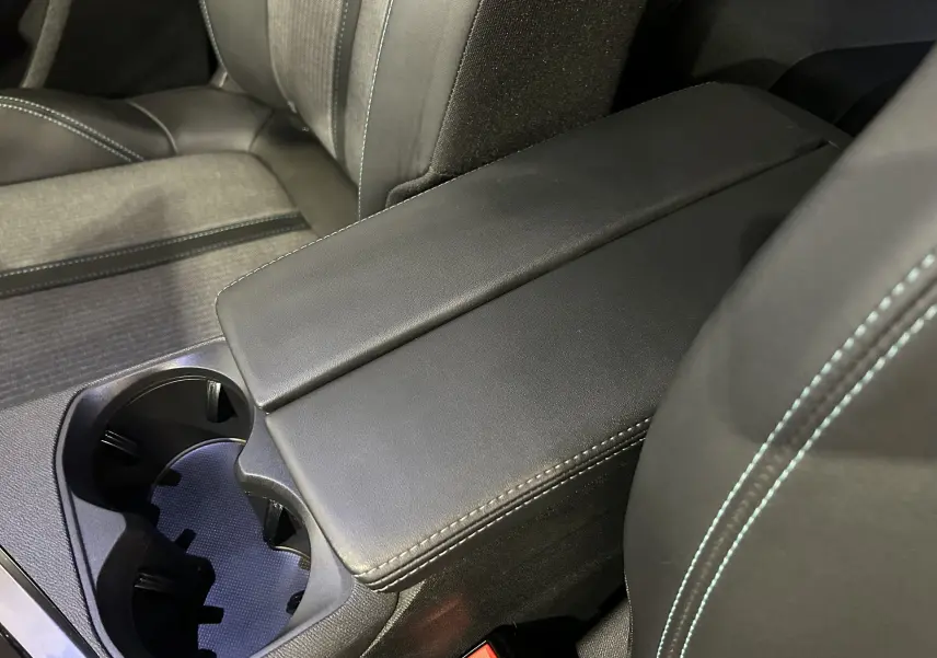 Détail de l’accoudoir central noir avec surpiqûres bleues et porte-gobelets du Peugeot 3008 Hybrid 2024.