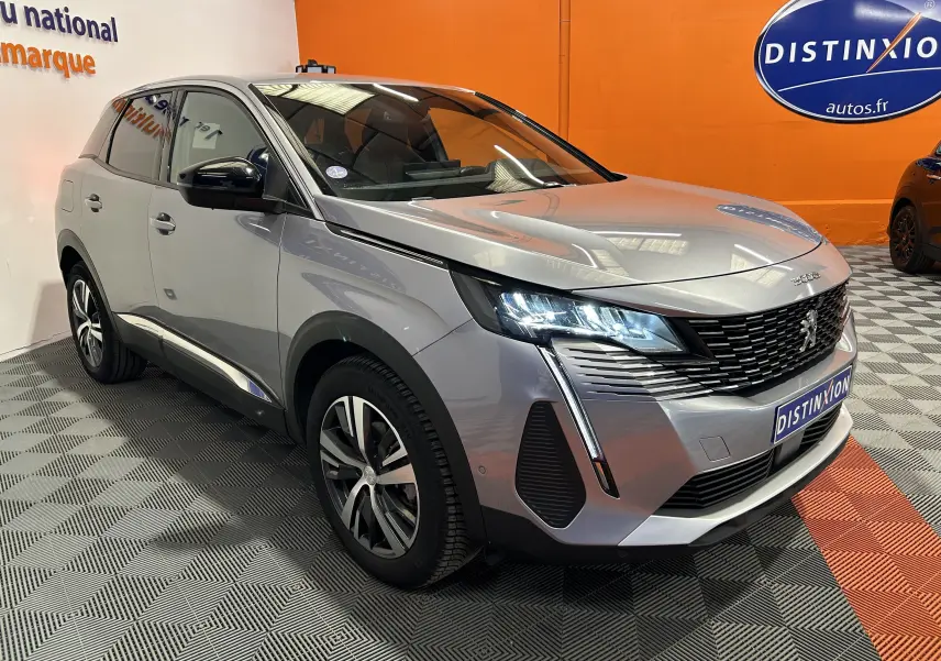 Peugeot 3008 gris en 3/4 avant droit, avec phares LED allumés et calandre noire distinctive, en intérieur showroom.