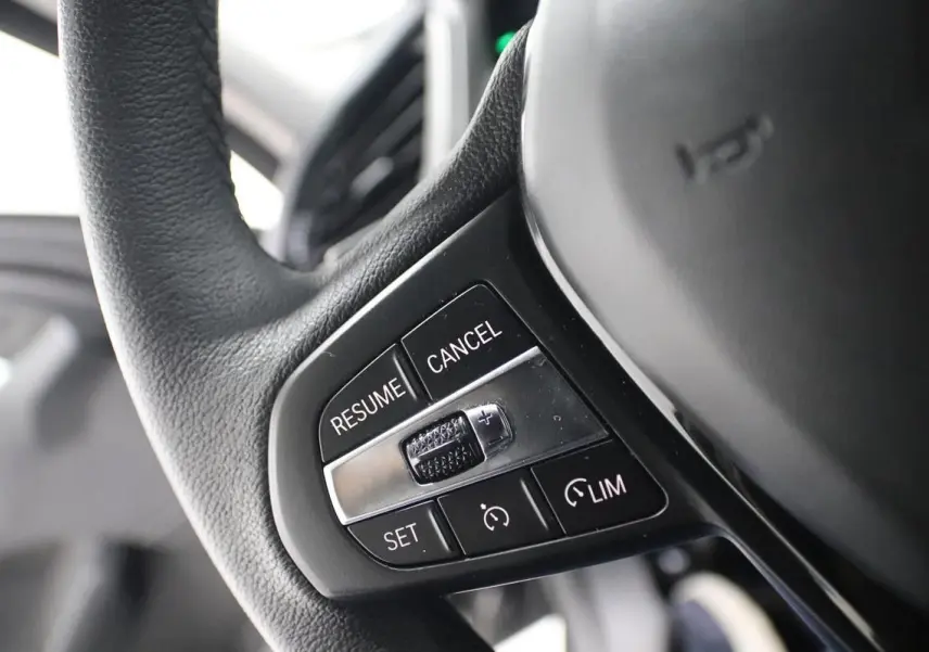 Gros plan sur les commandes du régulateur de vitesse au volant noir d'une BMW Série 1 116d 2023.
