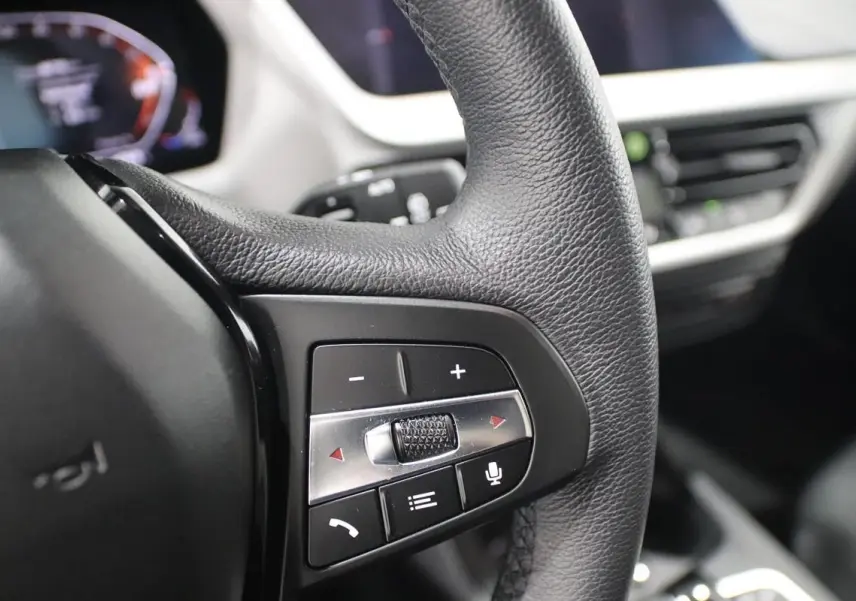 Gros plan sur les commandes du volant en cuir noir de la BMW Série 1 116d 2023 avec affichage numérique en arrière-plan.