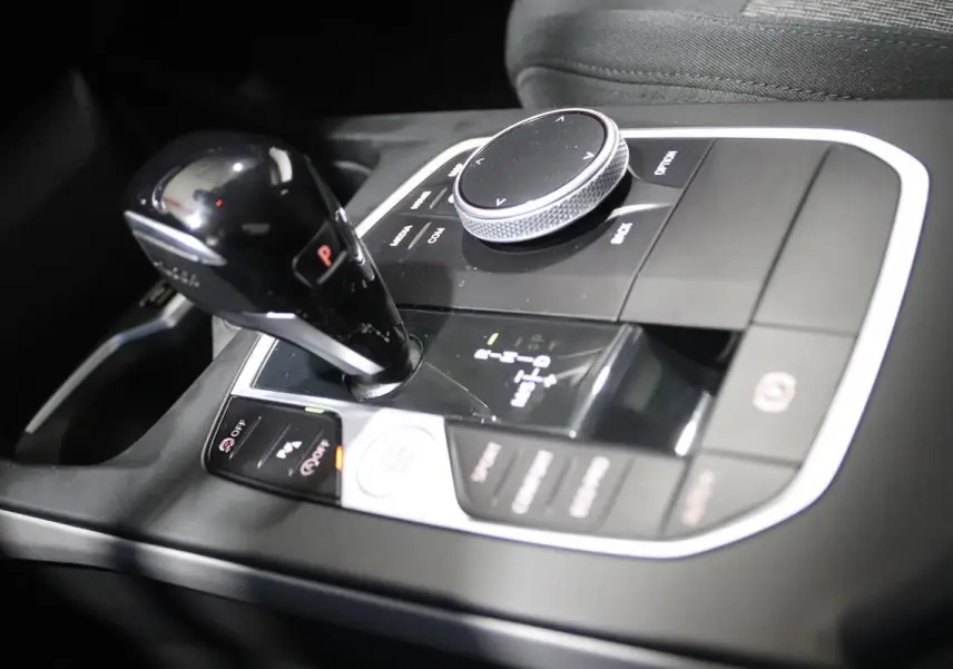 Gros plan sur la console centrale noire de la BMW Série 1 116d 2023 avec levier de vitesse automatique et molette de contrôle.