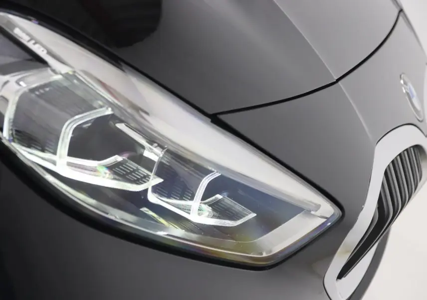 Gros plan sur le phare avant gauche d’une BMW Série 1 noire 2023, mettant en valeur la calandre et les lignes du capot.