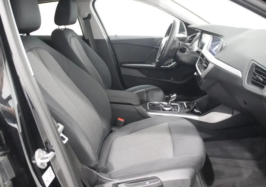 Vue intérieure côté gauche de la BMW Série 1 noire 116d 2023, montrant sièges tissu et console centrale avec boîte auto.