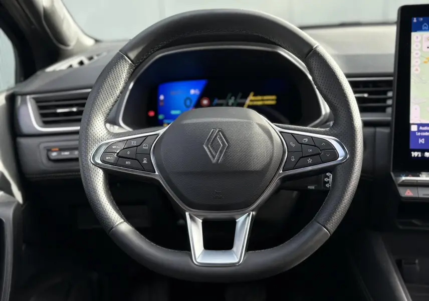 Volant en cuir noir perforé de la Renault SYMBIOZ 2025, avec commandes intégrées et tableau de bord numérique en arrière-plan.