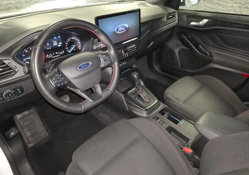Vue intérieure côté conducteur de la Ford Focus ST Line 2024, volant cuir noir avec surpiqûres rouges et écran tactile central.