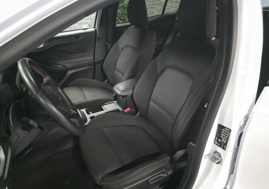 Vue intérieure côté conducteur de la Ford Focus blanche 2024, sièges tissu ST-Line noirs avec surpiqûres rouges.