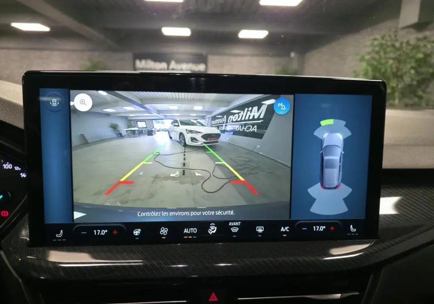 Écran multimédia montrant la caméra de recul avec vue 3/4 avant d'une Ford Focus blanche en intérieur.
