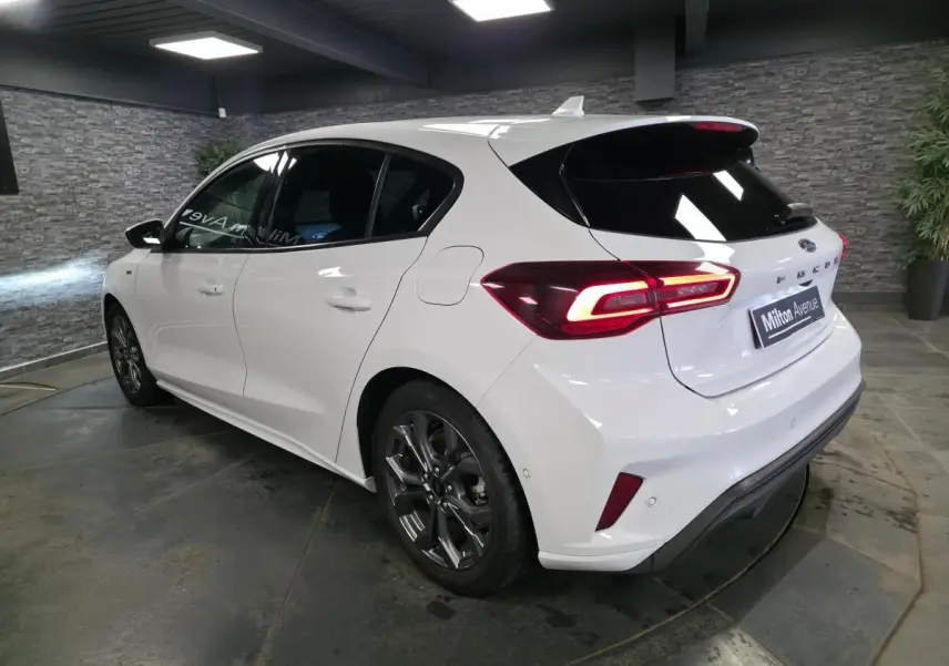 Ford Focus blanche 2024 vue 3/4 arrière droit, feux arrière LED allumés et jantes alliage 17 pouces.