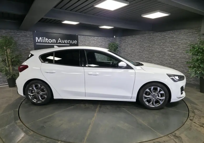 Ford Focus blanche 2024 vue de profil côté gauche, jantes alliage 17 pouces et vitres surteintées.