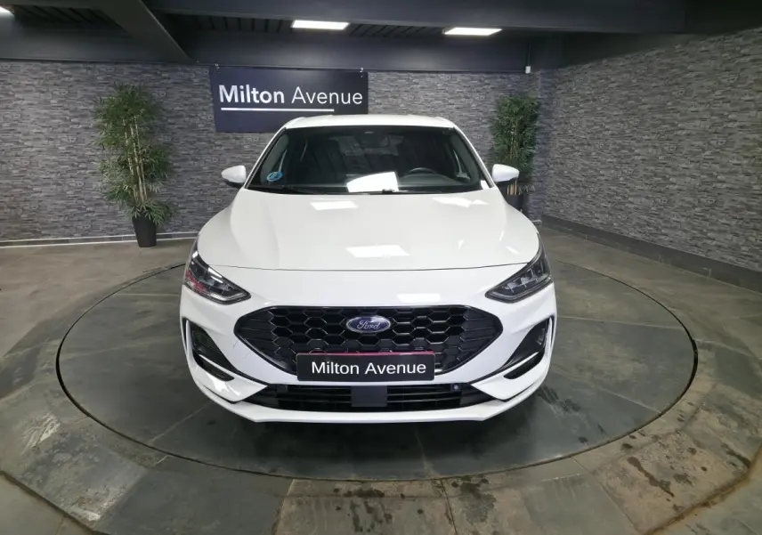 Vue avant d'une Ford Focus blanche 2024 avec calandre noire hexagonale et phares LED dans un showroom.