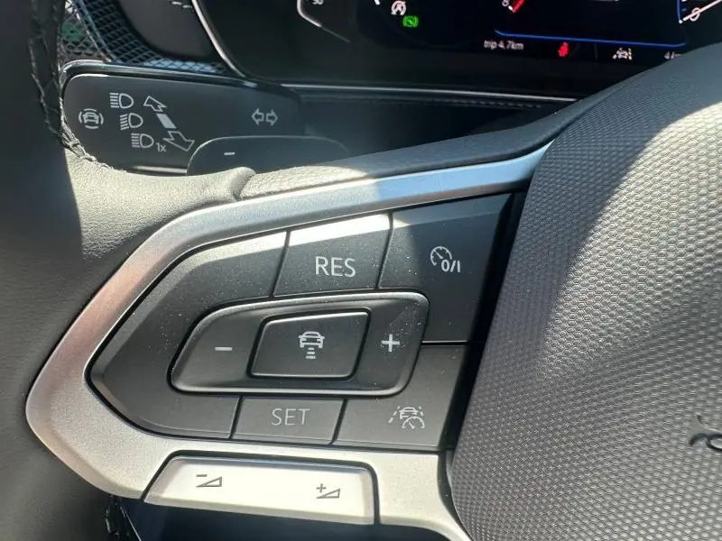 Gros plan sur les commandes au volant du Volkswagen T-Cross gris cendré, avec boutons de régulateur de vitesse et assistance conduite.