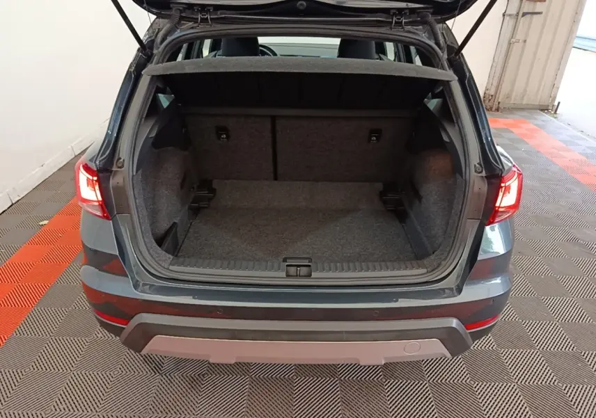 Vue arrière du coffre ouvert d'un SEAT Arona gris clair, intérieur spacieux et tapis gris visible.