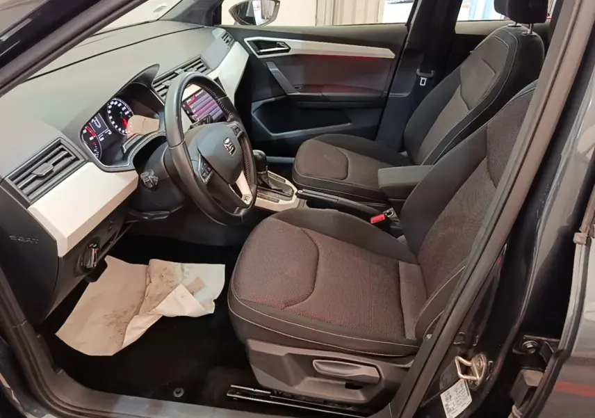 Vue intérieure côté conducteur de la SEAT Arona gris clair 2019, avec tableau de bord et sièges tissu noirs.