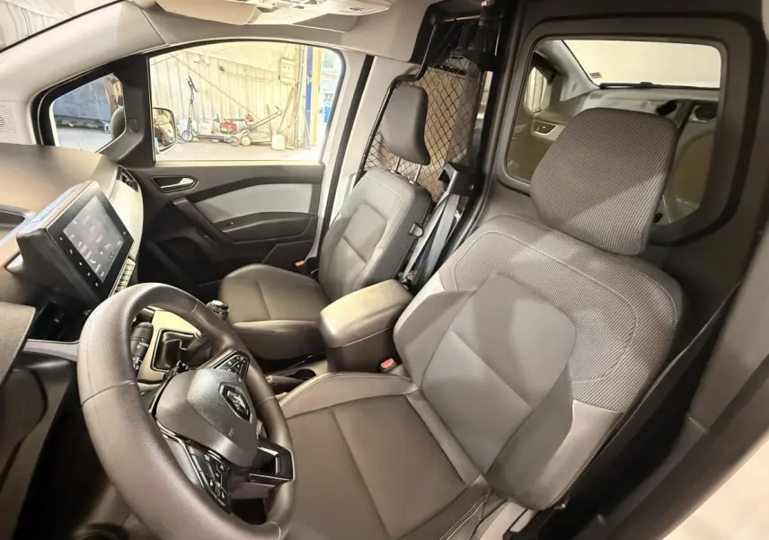 Vue intérieure côté conducteur du Renault Kangoo blanc 2022, avec volant, sièges gris et cloison métallique de séparation.