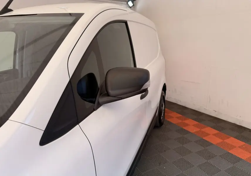 Vue de côté droit d’un Renault Kangoo blanc 2022, avec rétroviseur noir, stationné sur un sol à damiers gris et orange.