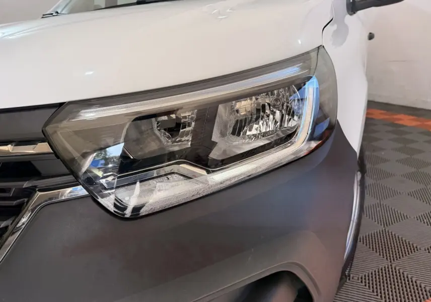 Gros plan sur le phare avant droit du Renault Kangoo blanc 2022 avec calandre noire et pare-chocs gris.