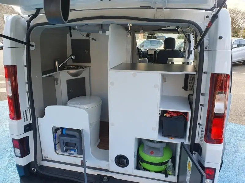 Vue arrière ouverte du Renault Trafic Fourgon blanc glacier aménagé en van avec kitchenette et rangements visibles.