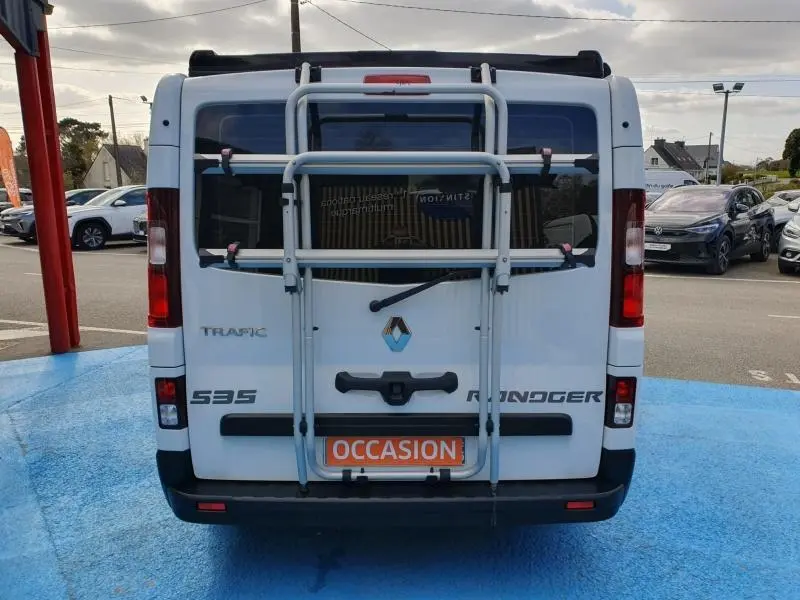 Vue arrière d’un Renault Trafic Fourgon blanc Glacier avec porte-vélos fixé sur les portes vitrées arrière.