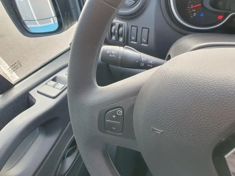 Gros plan sur le volant et la commande des phares du Renault Trafic Fourgon blanc, côté gauche avec rétroviseur visible.