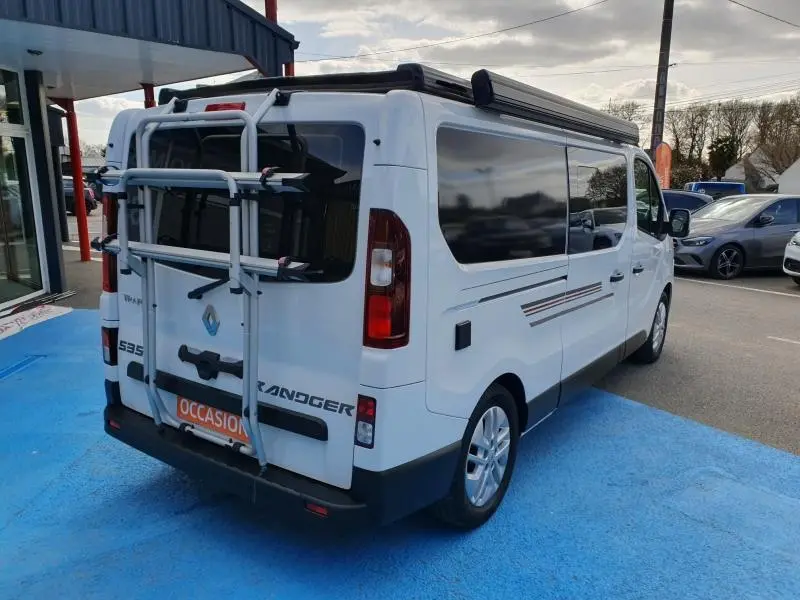 Vue 3/4 arrière droite du Renault Trafic Fourgon blanc Glacier avec porte-vélos et vitres teintées.