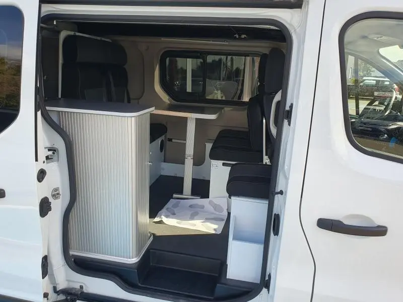 Vue latérale droite du Renault Trafic Fourgon blanc Glacier 2022, intérieur aménagé avec banquettes et table centrale.