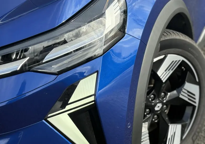 Gros plan sur l'avant droit bleu Iron du Renault SYMBIOZ, mettant en valeur le phare LED et la jante 18" Gravity.