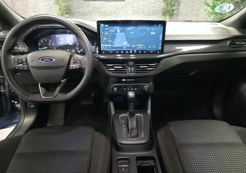 Vue intérieure avant de la Ford Focus 2024 bleu, volant ST Line, écran tactile central et levier de vitesses automatique.