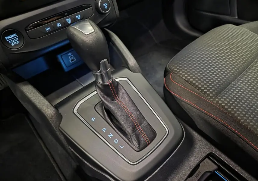 Gros plan sur la console centrale de la Ford Focus 2024 ST Line, levier de vitesses automatique avec surpiqûres rouges et siège tissu à motifs.