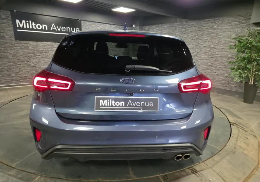 Vue arrière d'une Ford Focus 2024 bleu azur avec feux LED allumés et double sortie d'échappement sport.