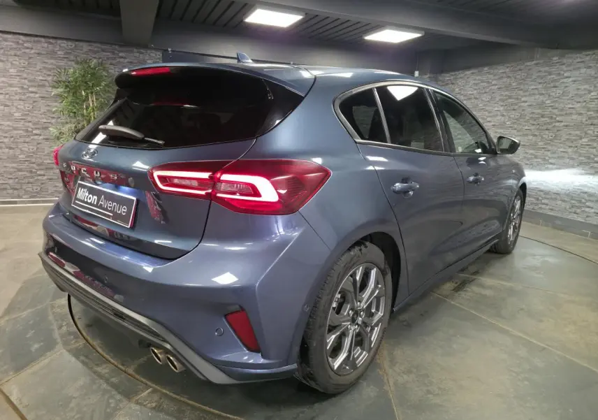 Vue 3/4 arrière droite d'une Ford Focus 2024 bleu métallisé avec feux arrière LED et double sortie d'échappement sport.