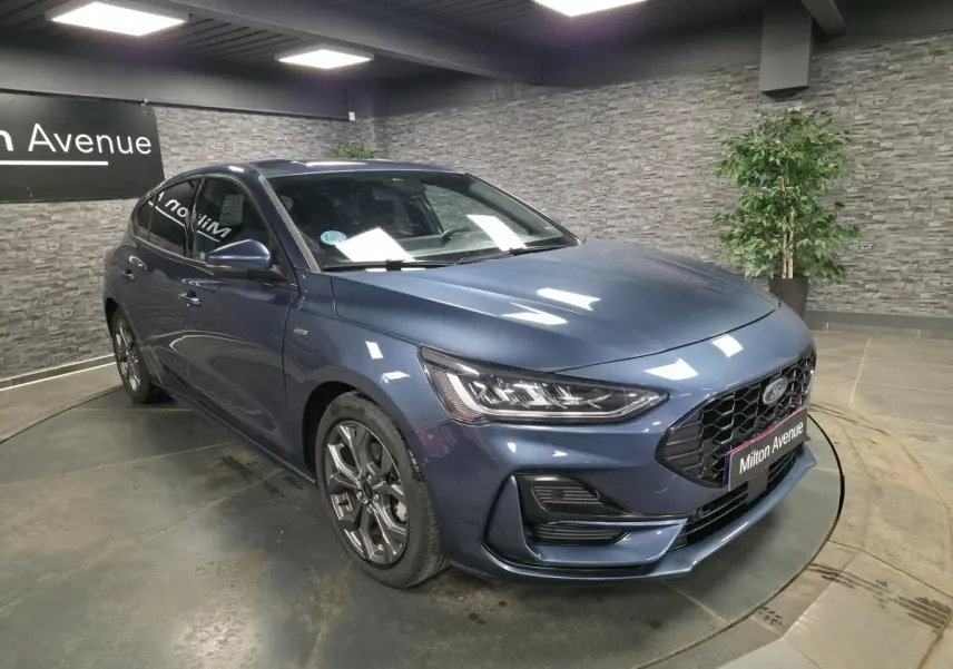 Ford Focus 2024 bleu métallisé vue 3/4 avant avec calandre noire et jantes alliage 17 pouces dans un showroom.