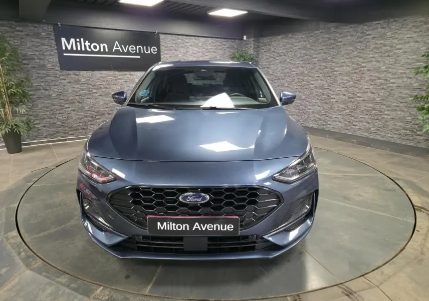 Vue avant d'une Ford Focus 2024 bleu métallisé avec calandre noire ST-Line et phares LED, en intérieur showroom.