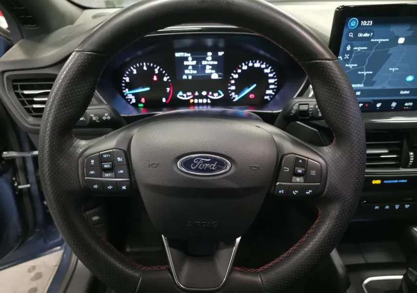Vue intérieure centrée sur le volant ST-Line en cuir noir avec surpiqûres rouges et tableau de bord numérique de la Ford Focus 2024.