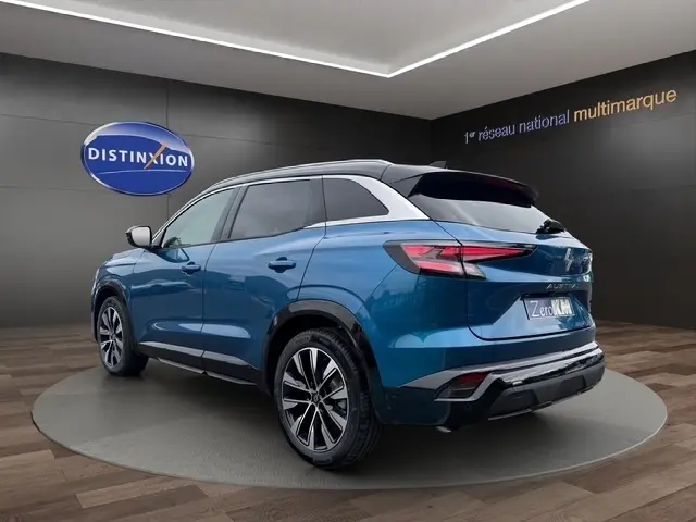 Vue 3/4 arrière droite du Renault Austral bleu bi-ton avec hayon motorisé et jantes alliage, en intérieur showroom.