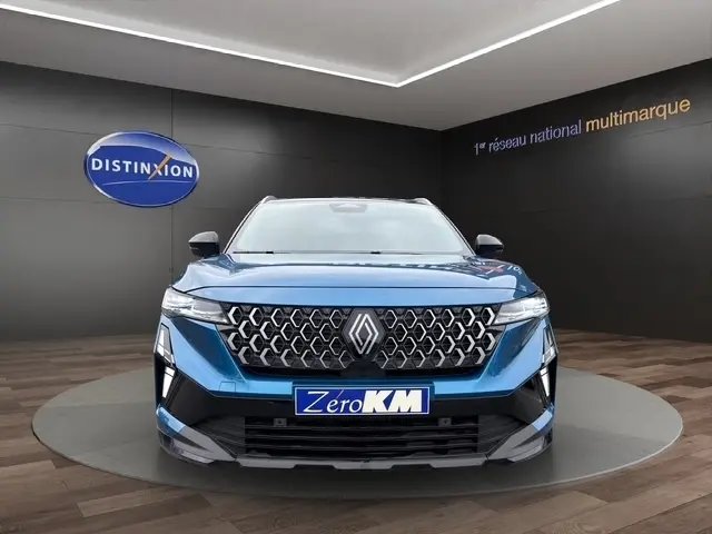 Vue frontale du Renault Austral bleu avec calandre hexagonale distinctive et hayon motorisé en arrière-plan.