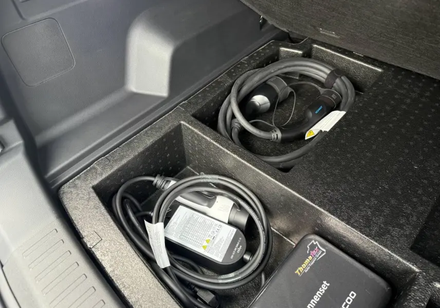 Coffre ouvert du JAECOO J7 hybride, montrant le rangement noir avec câbles de recharge et accessoires.