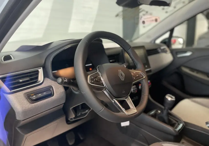 Intérieur de la Renault Clio 2025, vue côté conducteur sur le volant multifonction et la console centrale avec levier manuel.