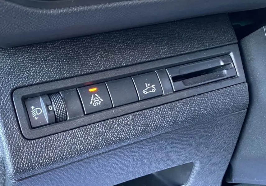 Gros plan sur les commandes intérieures noires du tableau de bord, avec bouton hayon main libre et témoin allumé.