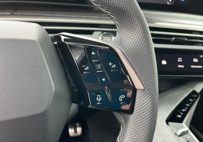 Gros plan sur les commandes multifonctions du volant cuir perforé du Peugeot 5008 Hybrid gris titane.