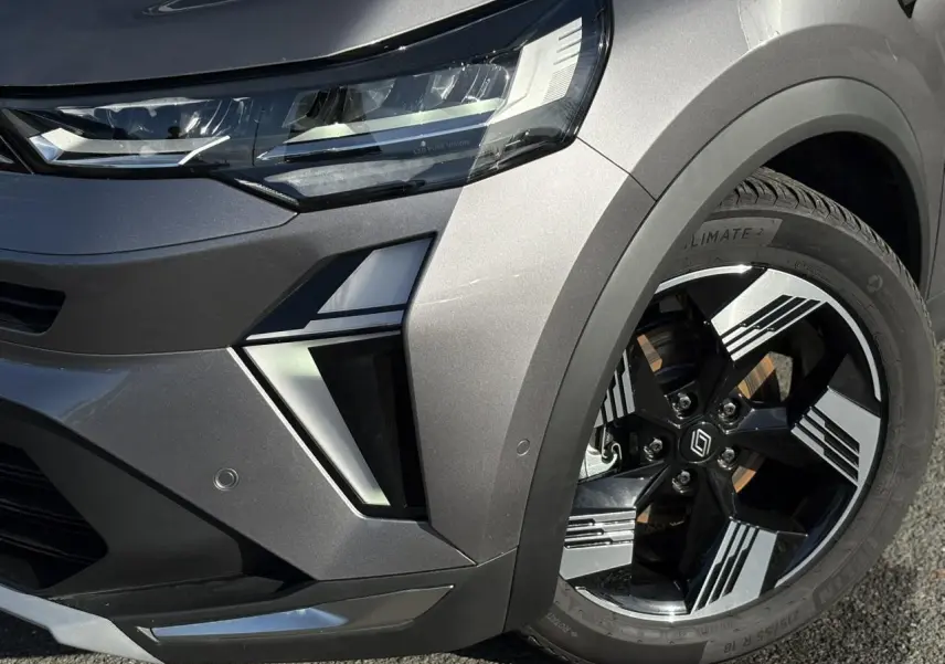 Gros plan sur l'avant droit gris Cassiopée du Renault Symbioz 2025, mettant en valeur le phare LED et la jante 18 pouces design.