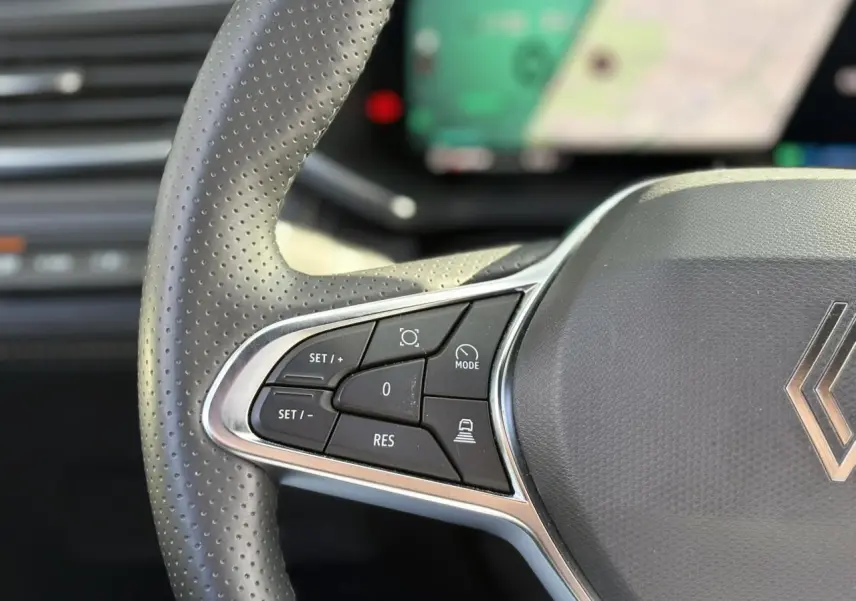 Gros plan sur les commandes du volant en cuir perforé gris du Renault Symbioz 2025 avec affichage numérique flou en arrière-plan.