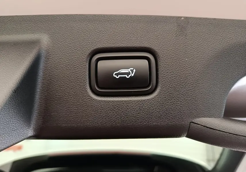 Bouton noir d'ouverture électrique du coffre sur la garniture intérieure d'un Hyundai Tucson blanc, vue rapprochée.