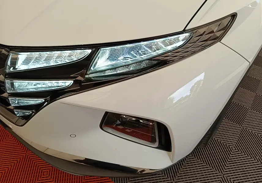 Gros plan sur l’avant droit blanc du Hyundai Tucson 1.6 Hybrid 230 Executive avec phares LED allumés.