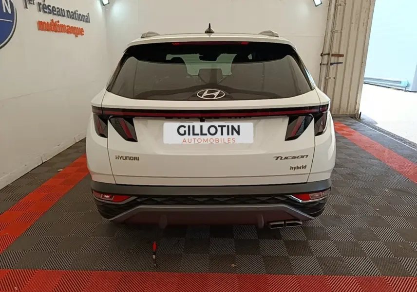 Vue arrière d'un Hyundai Tucson blanc hybride 2022 avec feux arrière LED et logo Hyundai visible.
