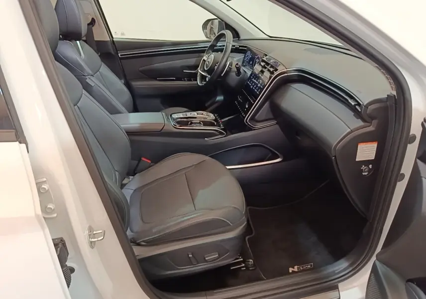 Vue intérieure côté conducteur du Hyundai Tucson blanc 2022, avec sièges cuir noirs et tableau de bord moderne.